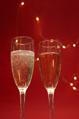Vertical image of two wine glasses against bright golden lights and red background