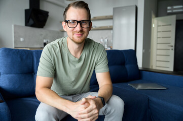 Fototapeta premium A head shot of a young happy man in casual shirt talking via video call, mentor, trainer conducts webinar, online class. Video meeting, virtual conference with an intelligent guy, webcam view
