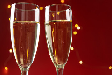 Closeup of two wineglasses and champagne against red background, golden shiny lights