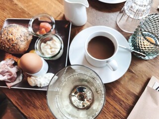 Table laid for breakfast outside in summer with various jams, bread, coffee, croissants, eggs, bacon muesli and orange juice