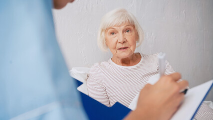 Fototapeta na wymiar blurred geriatrician writing prescription near aged woman