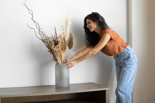 Modern minimalist home interior design. Young woman arranging dried plants in vase, creating cozy atmosphere in house