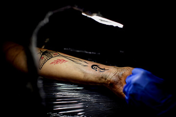 cropped shot of tattooing process on hand in salon. A professional tattoo artist introduces ink...