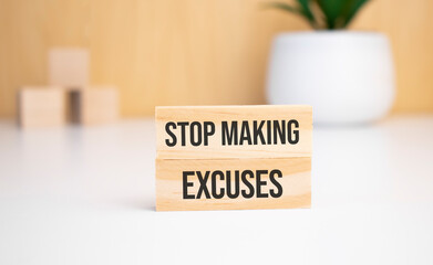 On a light background, wooden cubes and a wooden block with the text STOP MAKING EXCUSES. View from above