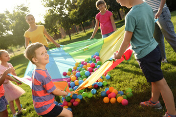 Group of children and teacher playing with rainbow playground parachute on green grass. Summer camp...