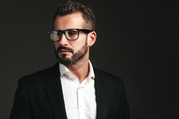 Closeup portrait of handsome confident stylish hipster lambersexual model. Sexy modern man dressed in elegant black suit. Fashion male posing in studio on dark background. In spectacles