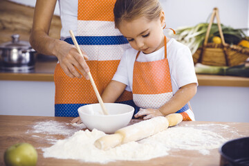 Happy woman and her daughter are kneading the dough and baking cookies for a delicious family feasting. Christmas, New year, Thanksgiving, Anniversary, Mothers Day. Healthy meal cooking concept