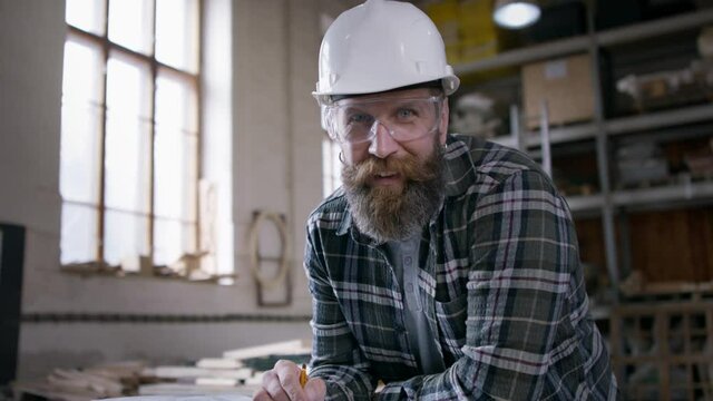 Male carpenter in protective goggles and helmet sketching desing of his product, looking at camera. Small business concept.