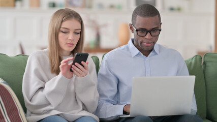 Interracial Couple Using LAptop and Smartphone Separately