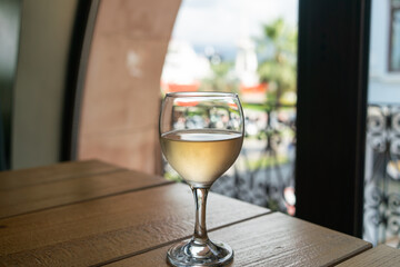 Close-up shot of a glass of cold white wine on a hot summer day on a wooden table against the background of an oval window and a forged metal lattice