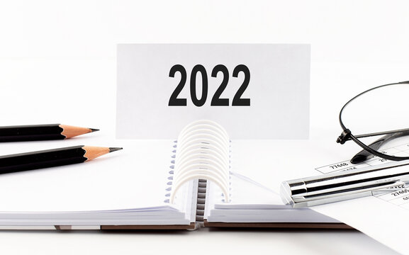 Text 2022 on paper card,pen, pencils, glasses,financial documentation on table - business concept