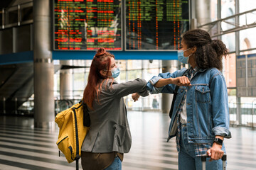 Young multiracial women in face masks elbow bumping at train station