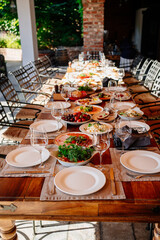 big wooden table served with plates with salad and snacks on the open terrace
