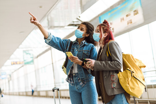 Young multiracial women in face masks using cellphones at train station