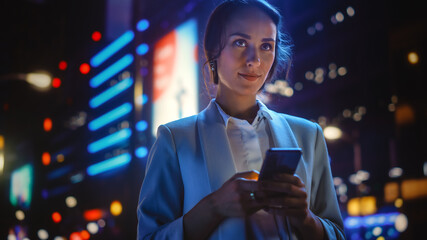 Beautiful Young Woman Using Smartphone Standing on the Night City Street Full of Neon Light....