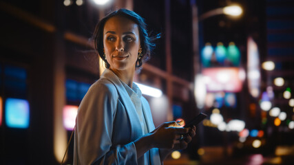 Beautiful Young Woman Using Smartphone Walking Through Night City Street Full of Neon Light....