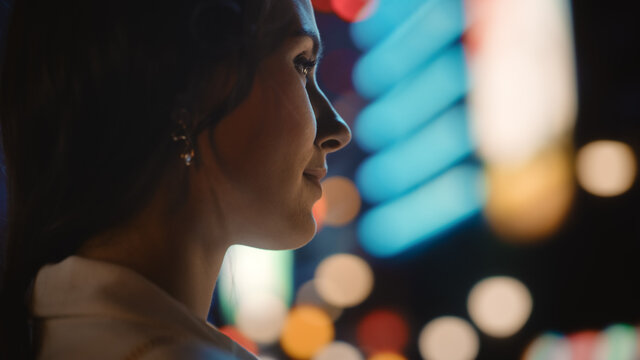 Beautiful Young Woman Walking Through Night City Street Full of Neon Lights and Entertainment Venues. Smiling Attractive Thoughtful Independent Woman Traveling. Over the Shoulder Shot.