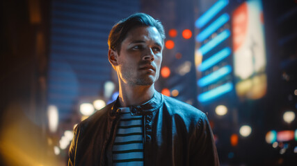 Portrait of Handsome Serious Man Standing, Looking Around Night City with Bokeh Neon Street Lights...