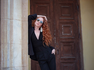Redhead woman in black suit walks in the spring city - 455473441