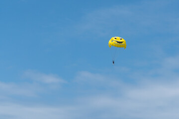 Parachutist flies in the blue sky with white clouds on a parachute in the form of a cheerful smiley