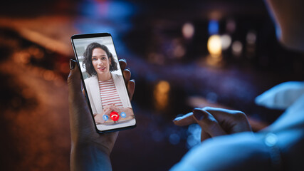 Close Up of a Female Using Smartphone for a Video Call with Her African American Female Colleague at Night City Street Full of Neon Light. Freelancer Making a Call with Manager Over the Internet.