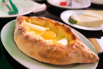 Georgian national dish adjarian khachapuri with egg, butter and cheese in a white plate on a table in a restaurant