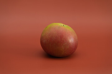 An apple on a uniform orange background. Vegetarian healthy food