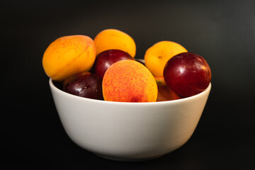Fruit with an apricot accent in a solid light bowl on a solid black surface. Healthy vegetarian food