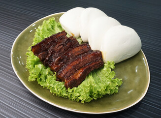 braised pork belly meat wrapped with mantou bun Chinese burger in plate on dark grey wood table asian dim sum halal food restaurant cuisine banquet menu for cafe