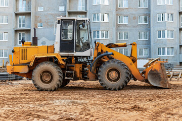 Fototapeta na wymiar Heavy wheel loader with a bucket at a construction site. Equipment for earthworks, transportation and loading of bulk materials - earth, sand, crushed stone.