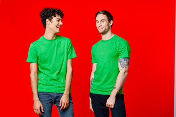 two friends in green t-shirts are standing side by side posing friendship red background