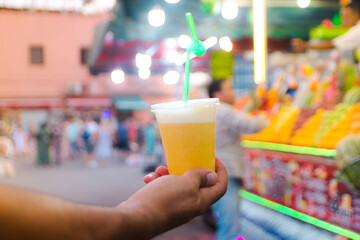 a hand holding a colorful sweet juice with blurred background and bokeh on sahat el fina marrakech...