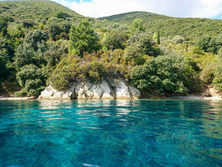 Turquoise clear calm Ionian Sea water with rocky wooded coast and wild nature of Lefkada island in Greece. Summer vacation idyllic travel destination
