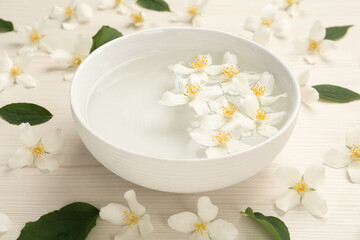Fototapeta na wymiar Bowl with water and beautiful jasmine flowers on white wooden table