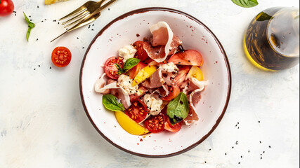Healthy fresh salad of vegetable tomatoes, cream cheese balls, prosciutto jamon and basil leaves. Food background for menu, recipe. Top view