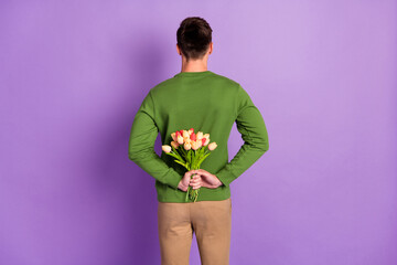 Back photo of young hide brunet guy hold flowers wear sweater isolated on purple background