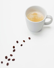 Kaffee in weißer Tasse mit Crema und Kaffeebohnen in minimalistischer Komposition