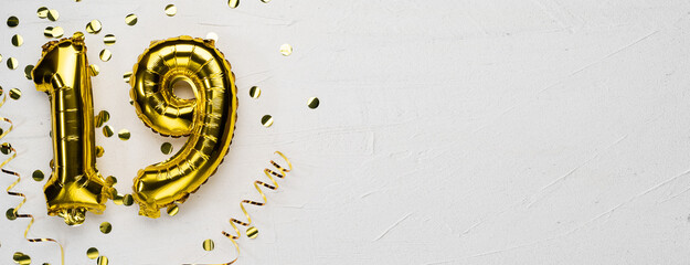 golden foil balloon number nineteen. Birthday or anniversary card with the inscription 19. gray concrete background.