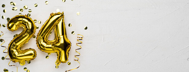 golden foil balloon number twenty four. Birthday or anniversary card with the inscription 24. gray concrete background.