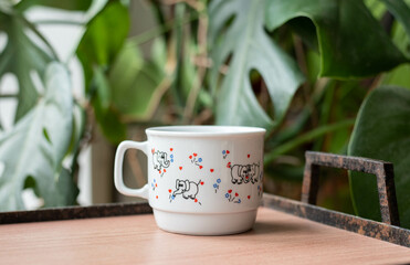 Mid-century modern porcelain mug with elephant pattern on a wooden table with tearing palm in the background