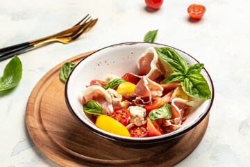 Fresh homemade salad with tomatoes, cream cheese balls, prosciutto jamon and basil leaves. Restaurant menu, dieting, cookbook recipe