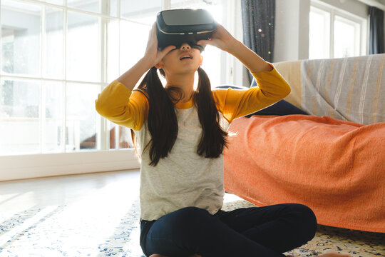 Smiling asian girl sitting in living room and using vr headset