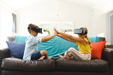 Caucasian brother and sister sitting on couch and using vr headsets in living room