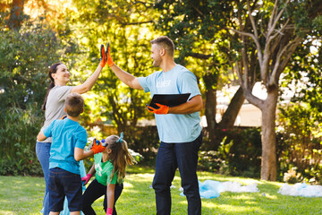 Caucasian parents, son and daughter high fiving, clearing up rubbish in the countryside