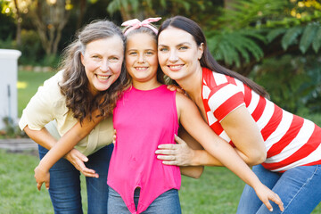 Portrait of smiling caucasian grandmother with adult daughter and granddaughter in garden