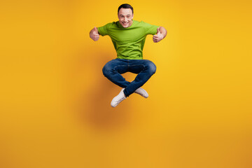 Fototapeta na wymiar Portrait of funky positive guy jump sport concept raise thumbs up on yellow wall