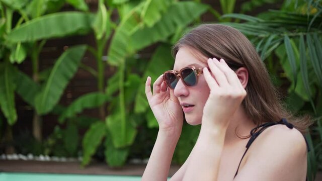A woman wears sunglasses by the pool. Resort in the jungle. Elegant lady posing