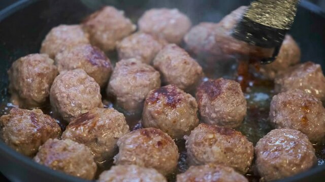 Frying meatballs in a black pan.