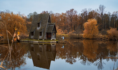 Panoramic image autumn scenic landscape. Wooden house by lake among forest, girl walking by wooden...