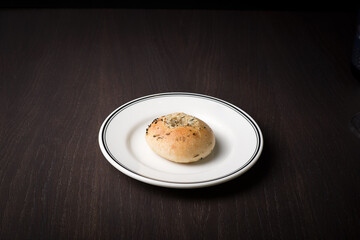 Bun with Provencal herbs on a white saucer and a dark oak table